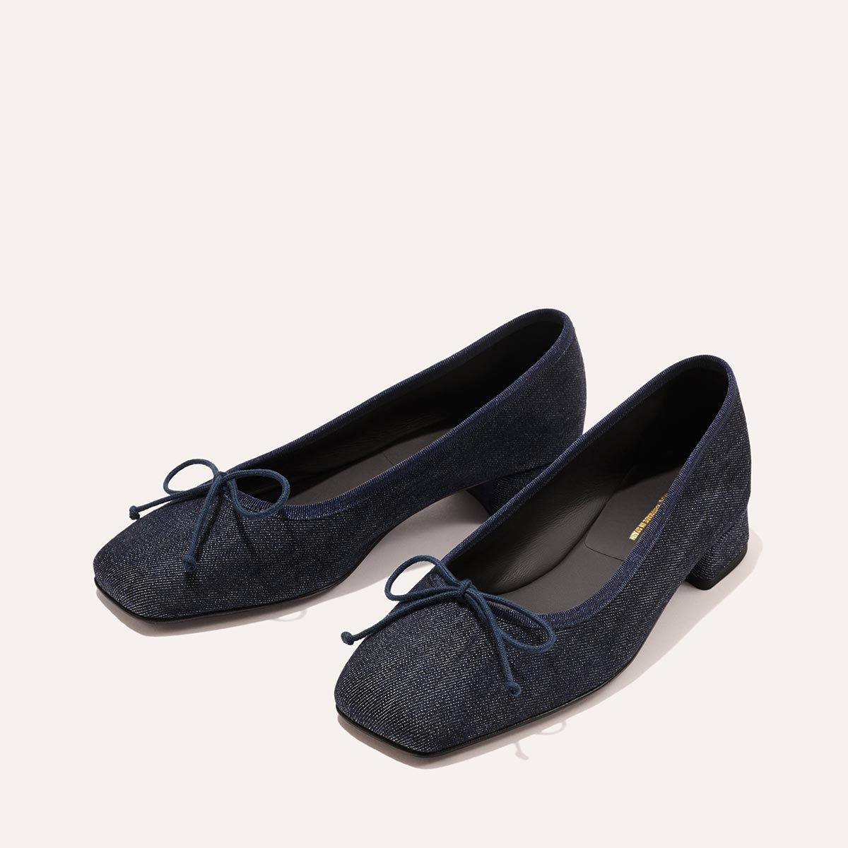 The Ada - Indigo Denim by margaux-development: navy blue fabric ballet pumps with low heels, square toes, and decorative bows, shown on a light background for a classic look.