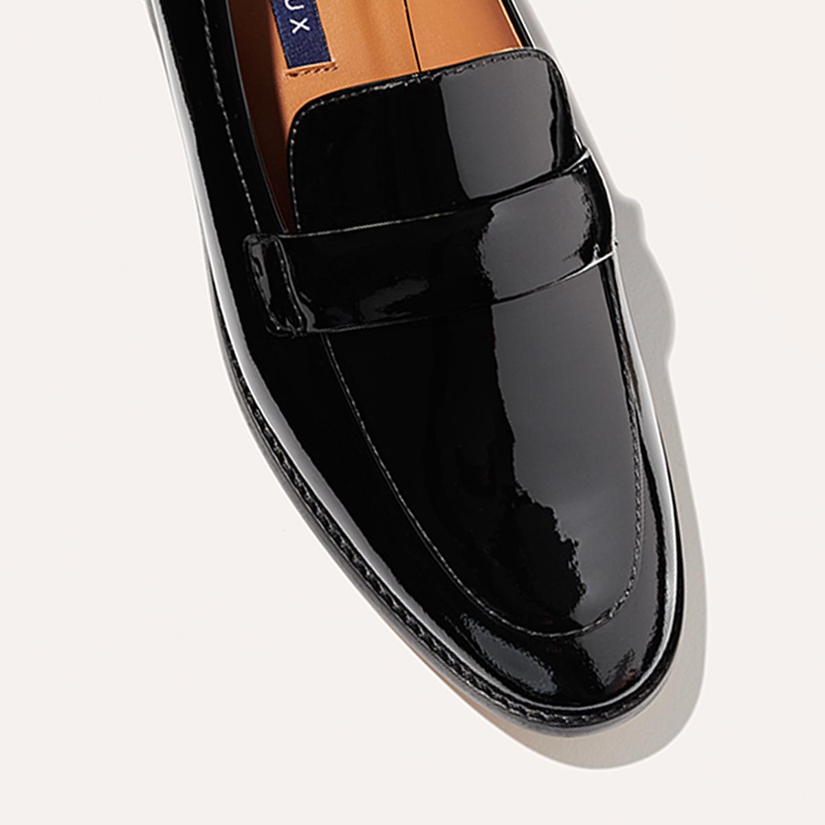 The Andie Loafer in shiny Black Patent, featuring a sleek structured design made from smooth Italian nappa leather with a minimalistic padded keeper detail.