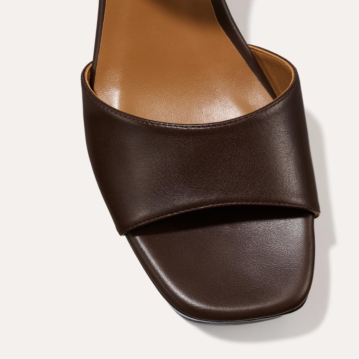 Close-up of The Bardi - Espresso Calf by margaux-development: a dark brown, open-toe sandal with a wide leather strap, square toe, tan footbed, and platform heel, shown from above against a light backdrop.