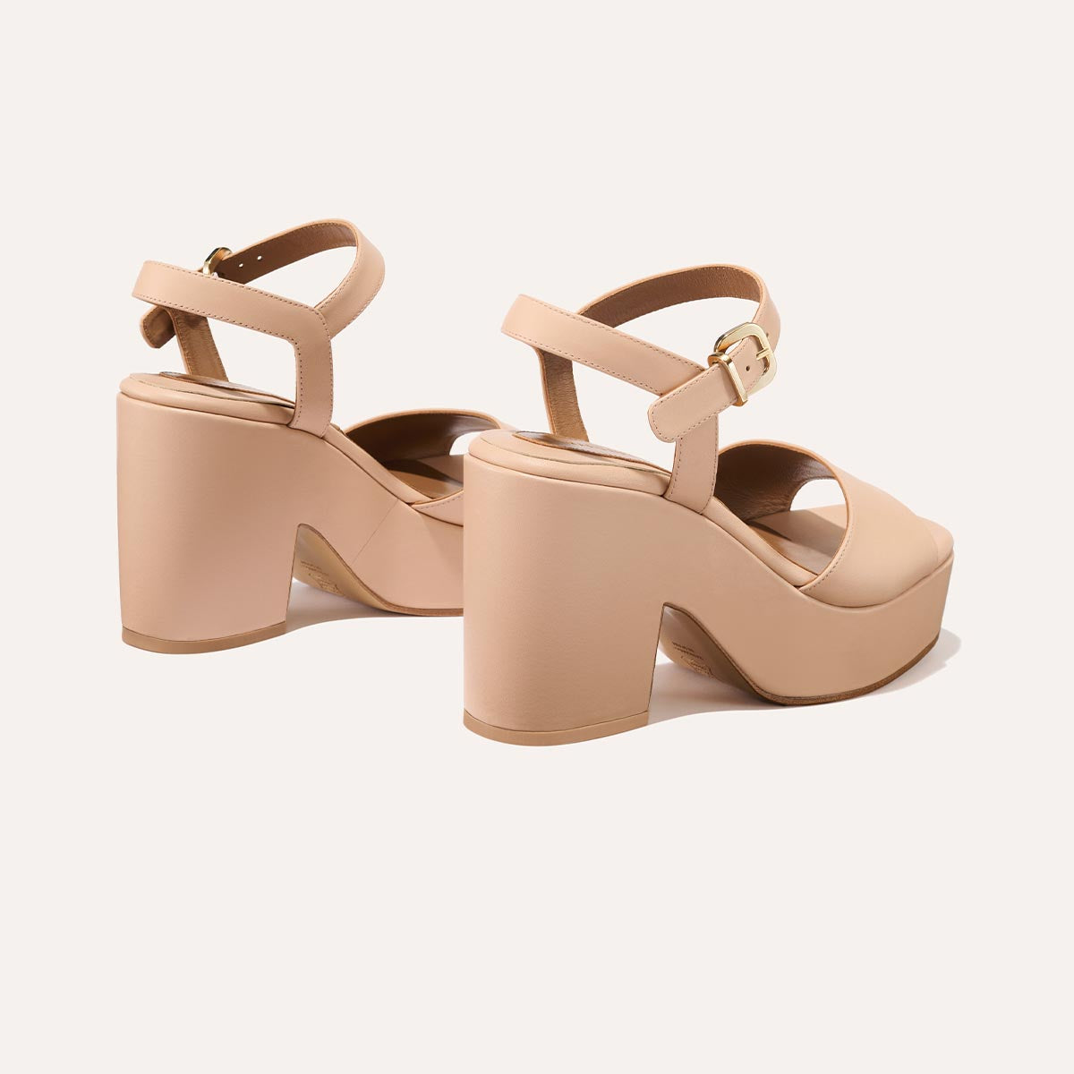 The Bardi - Petal Calf by margaux-development features nude platform sandals with chunky block heels, ankle straps, and gold buckles—radiating modern style and subtle disco glamour—displayed on a light background.