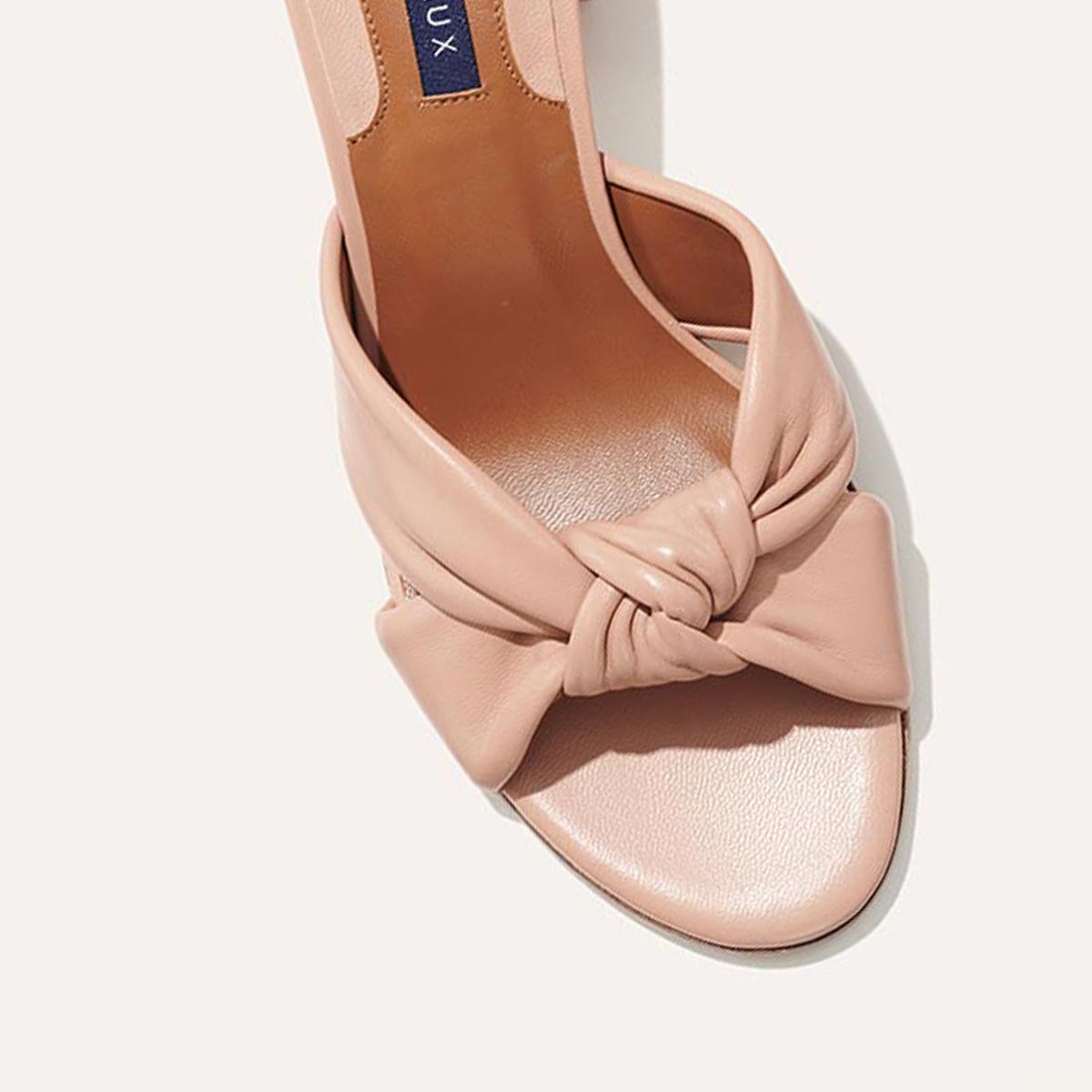 A close-up of The Carmine Mule - Rose Nappa by margaux-development, featuring a blush pink open-toe sandal with a plush knot front strap, set against a light background.