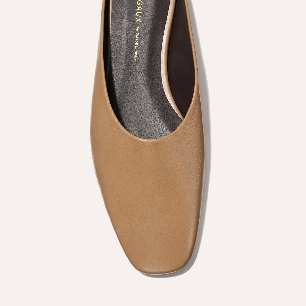 A close-up overhead view of Margaux’s The Clara - Praline Calf, a tan square-toe flat with a black insole and minimal design, set against a light background.