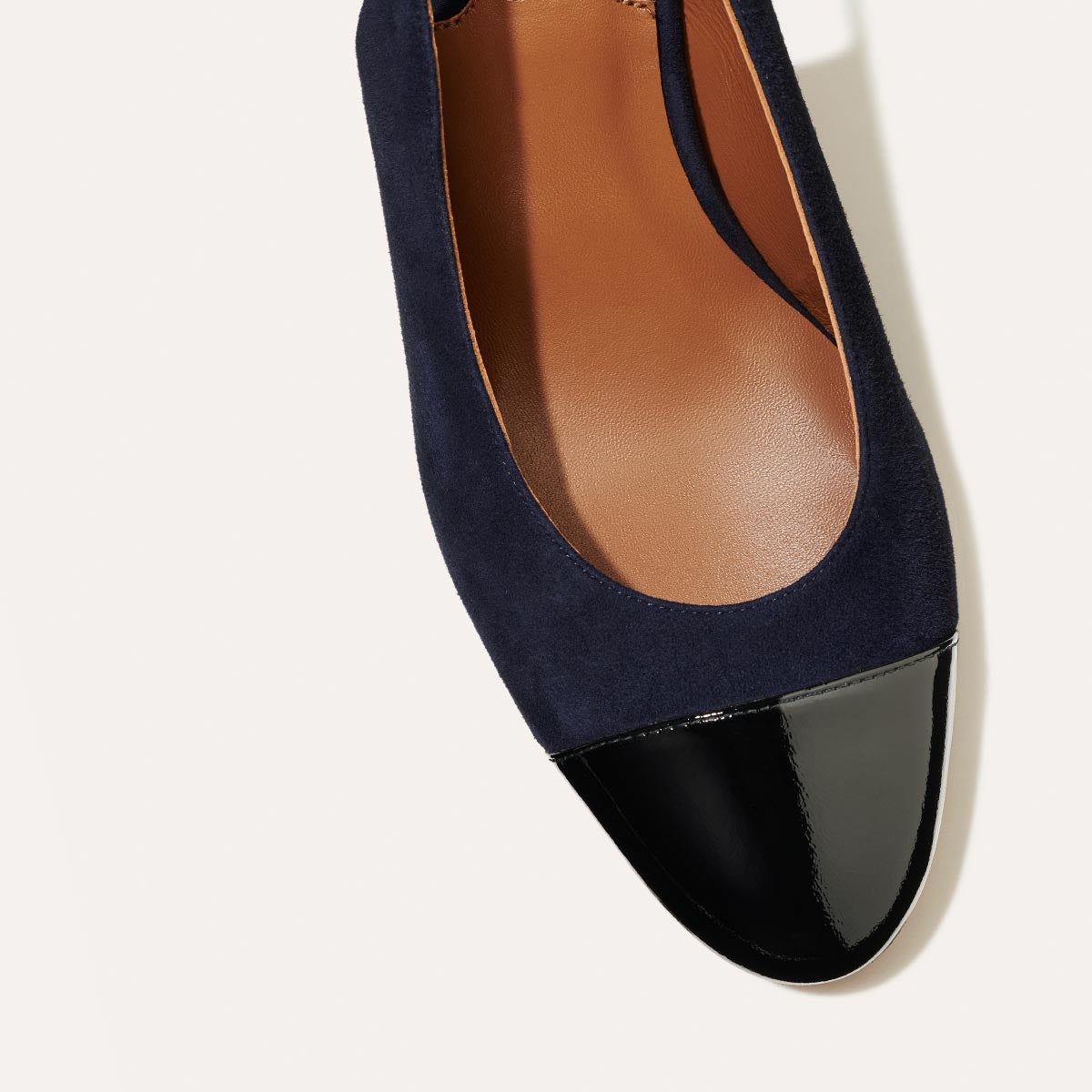 The Cluny Slingback in Navy Suede, featuring a sleek patent captoe detail with an adjustable buckle and a comfortable 2.5-inch black heel.