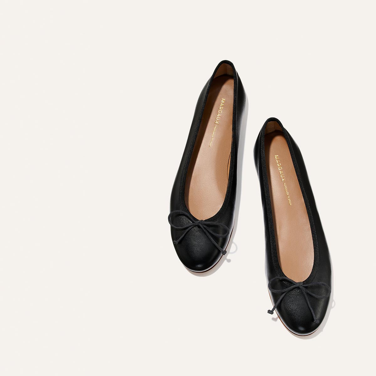 The Demi - Black Nappa by margaux-development: handmade black ballet flats from Spain, featuring small toe bows, shown from above on a light neutral background.
