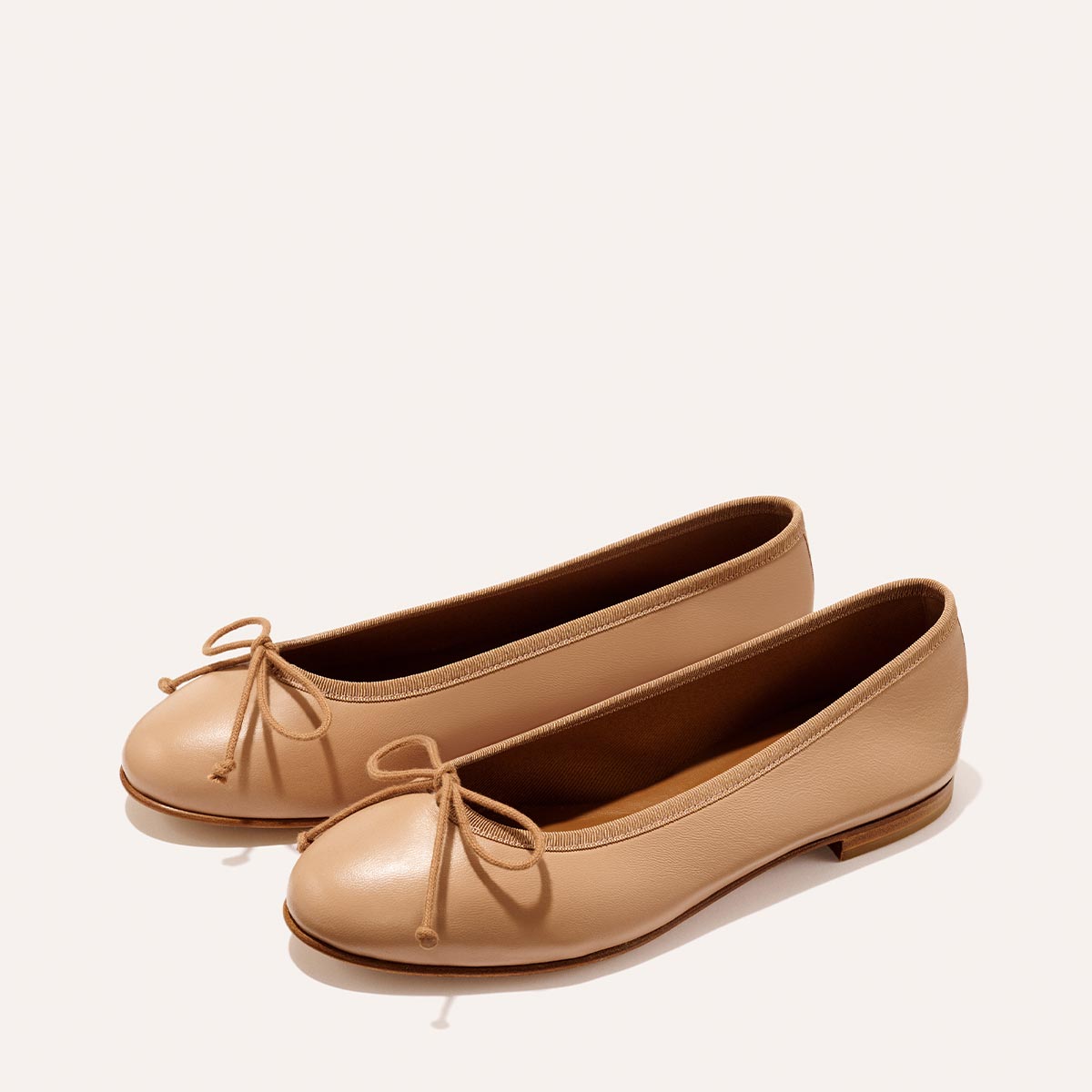 The Demi - Dune Nappa by margaux-development: beige leather ballet flats with rounded toes, brown soles, and petite front bows, shown on a plain light background.