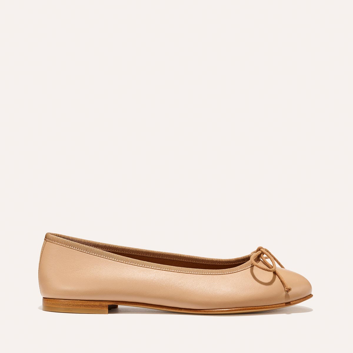 The Demi - Dune Nappa by margaux-development is a tan leather ballet flat featuring a small bow on the rounded toe, low heel, and classic design, shown on a neutral background.
