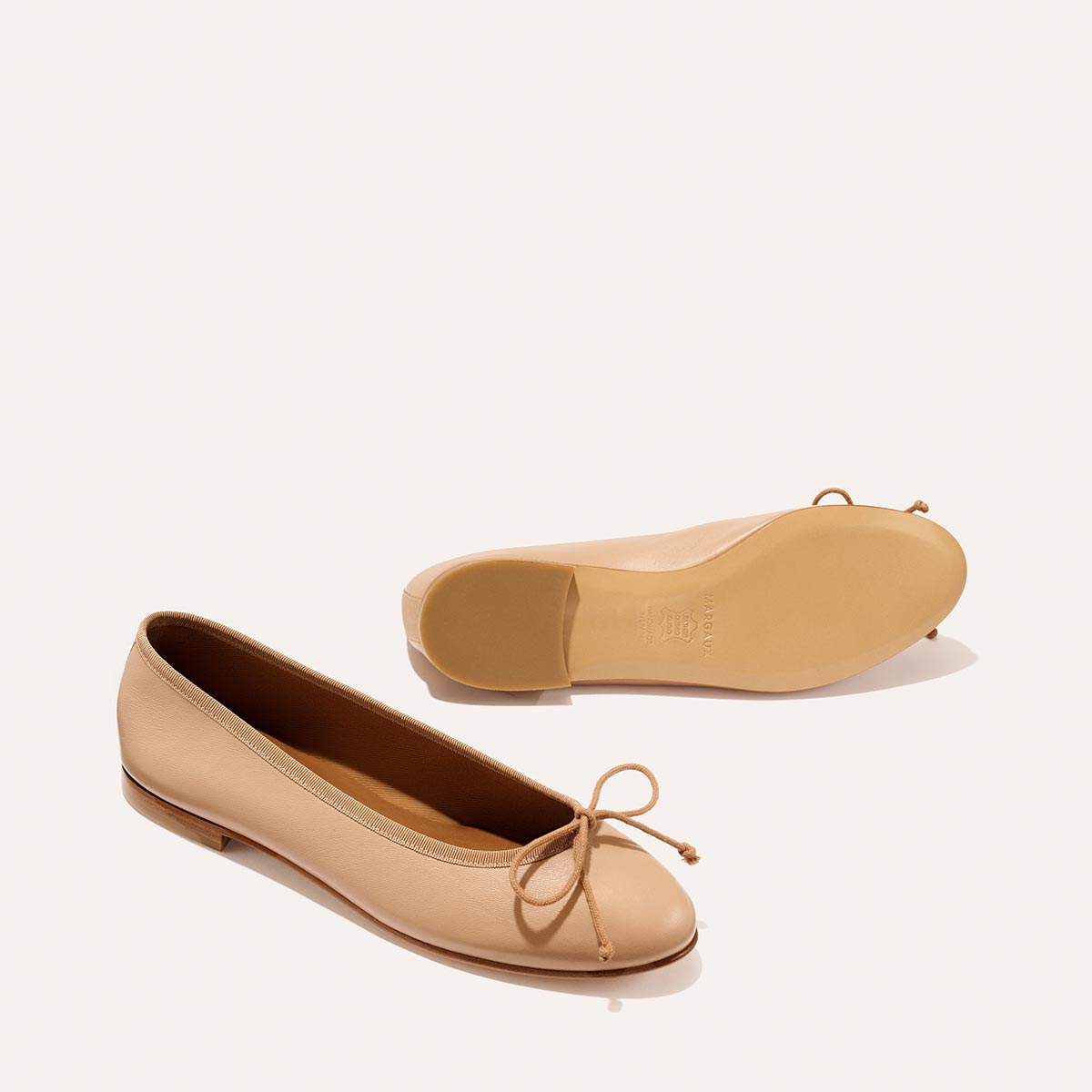 The Demi - Dune Nappa by margaux-development: beige leather ballet flats with rounded toes, small front bows, and flat soles. One shoe stands upright; the other lies on its side displaying the sole.