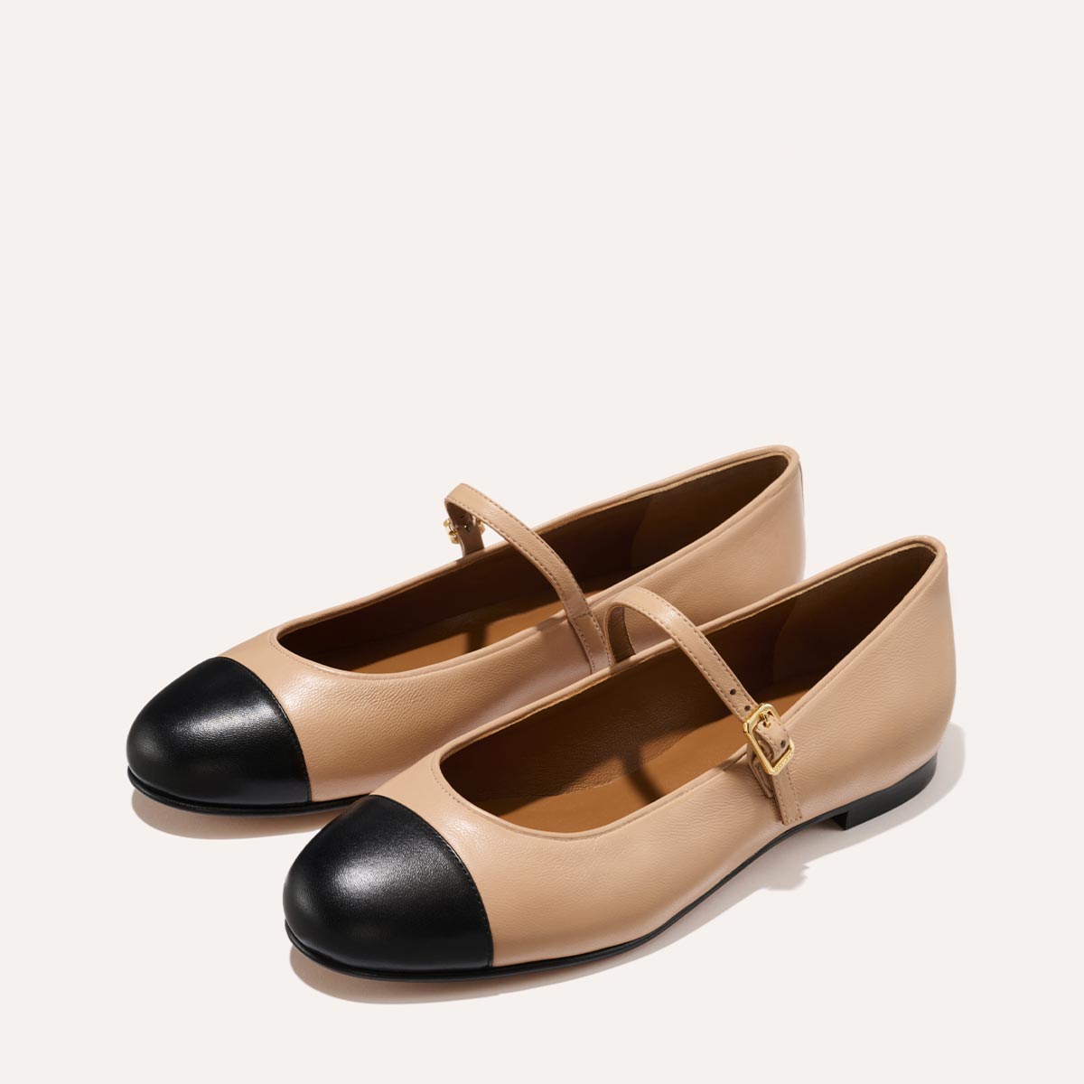 The Demi Jane in smooth Dune nappa leather, a ballet flat with a rounded toe, black cap-toe detail and an adjustable strap for a secure fit.