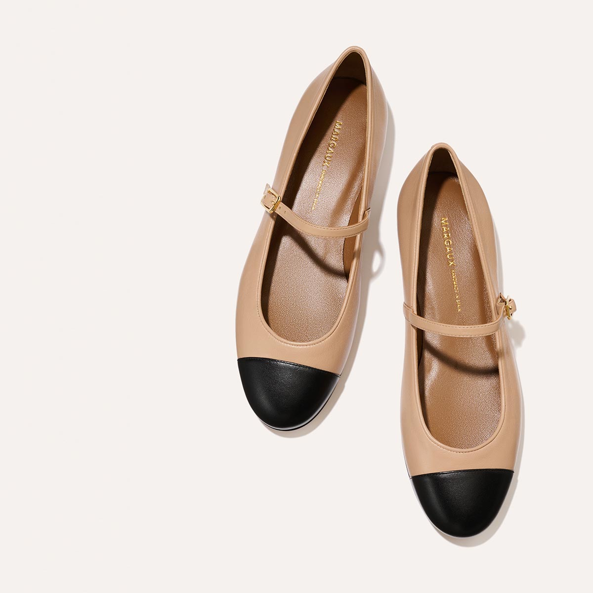 The Demi Jane in smooth Dune nappa leather, a ballet flat with a rounded toe, black cap-toe detail and an adjustable strap for a secure fit.