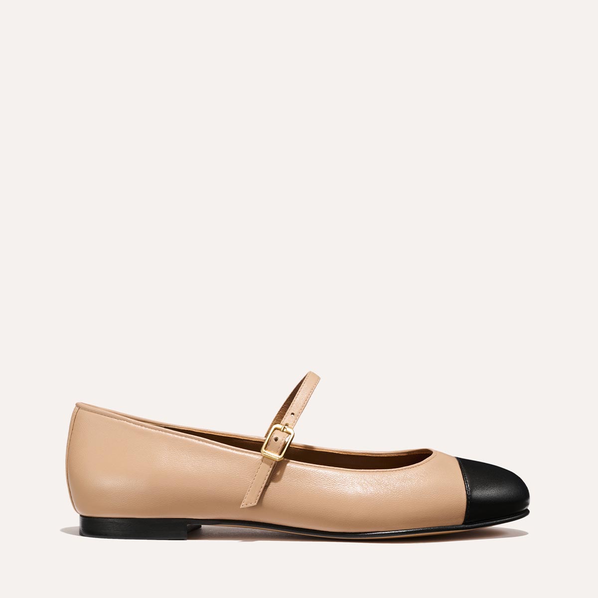 The Demi Jane in smooth Dune nappa leather, a ballet flat with a rounded toe, black cap-toe detail and an adjustable strap for a secure fit.