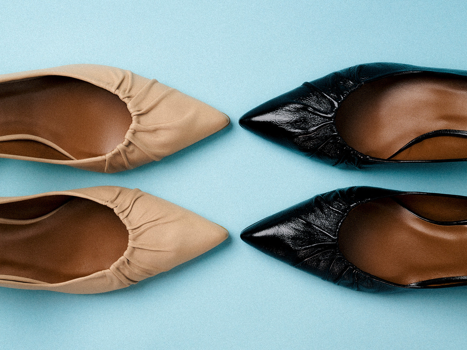 Two pairs of pointed-toe womens flats, one beige and one black, are arranged on a light blue background, with the toes of opposite colors facing each other diagonally.