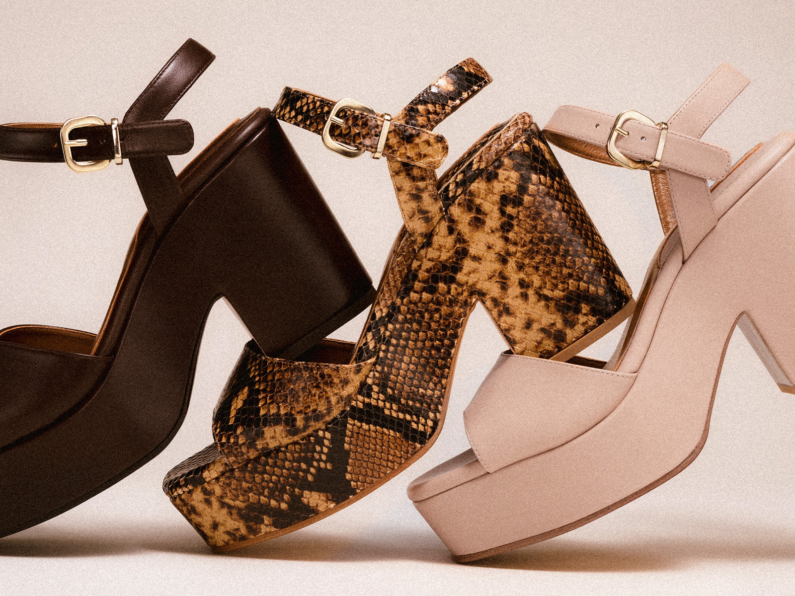 Three chunky platform heels are lined up side by side: one in dark brown leather, one in a snakeskin pattern, and one in beige leather, all featuring ankle straps with gold buckles.