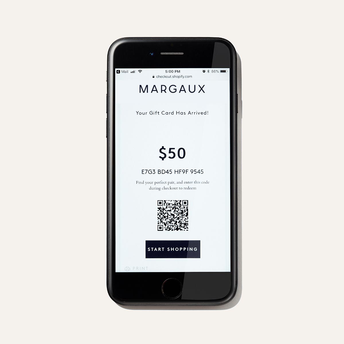 A smartphone displays The E-Gift Card by Margaux, showing a unique code and QR code. The message reads, Your Perfect Fit Gift Card Has Arrived! with a “Start Shopping” button below.