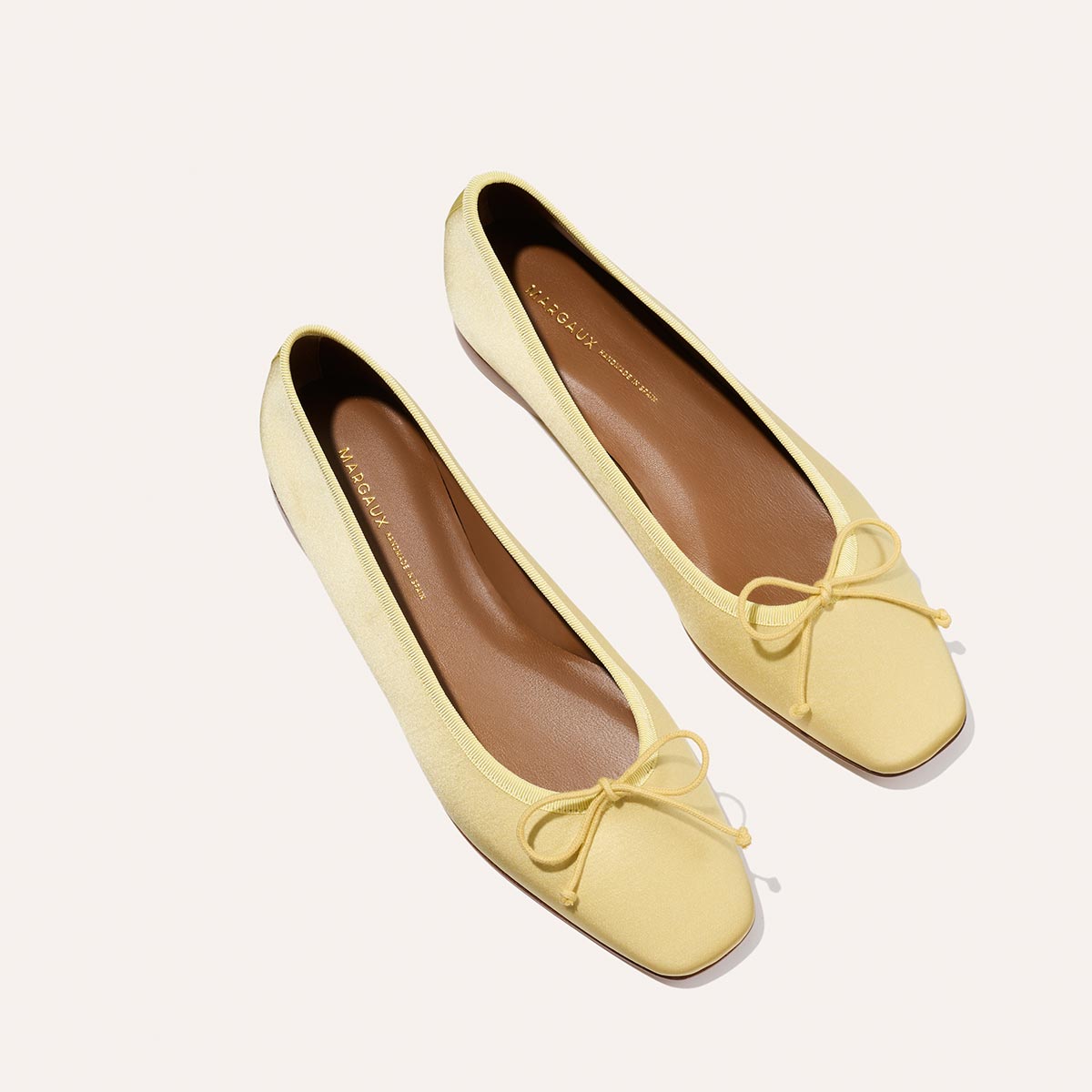 The Fonteyn - Butter Satin by Margaux: handcrafted yellow ballet flats with square toes and front bow details, designed for comfort and shown on a light background.