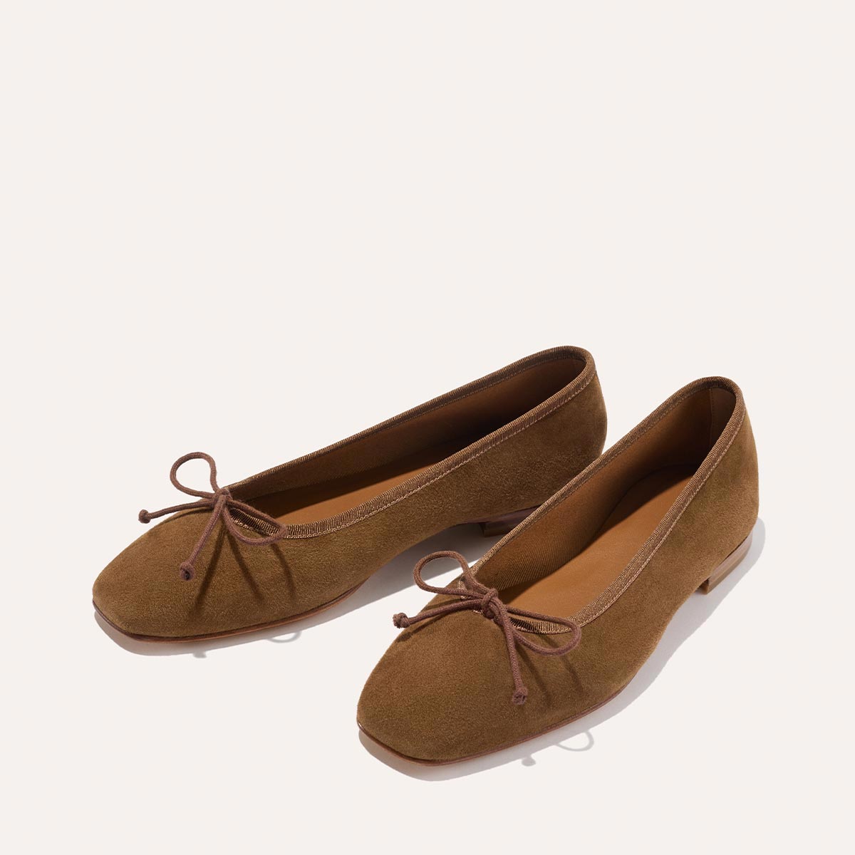 The Fonteyn - Cedar Suede by Margaux: handcrafted brown suede ballet flats with rounded toes, low heels, and slim brown bows on the front, displayed on a plain light background for ultimate comfort style.