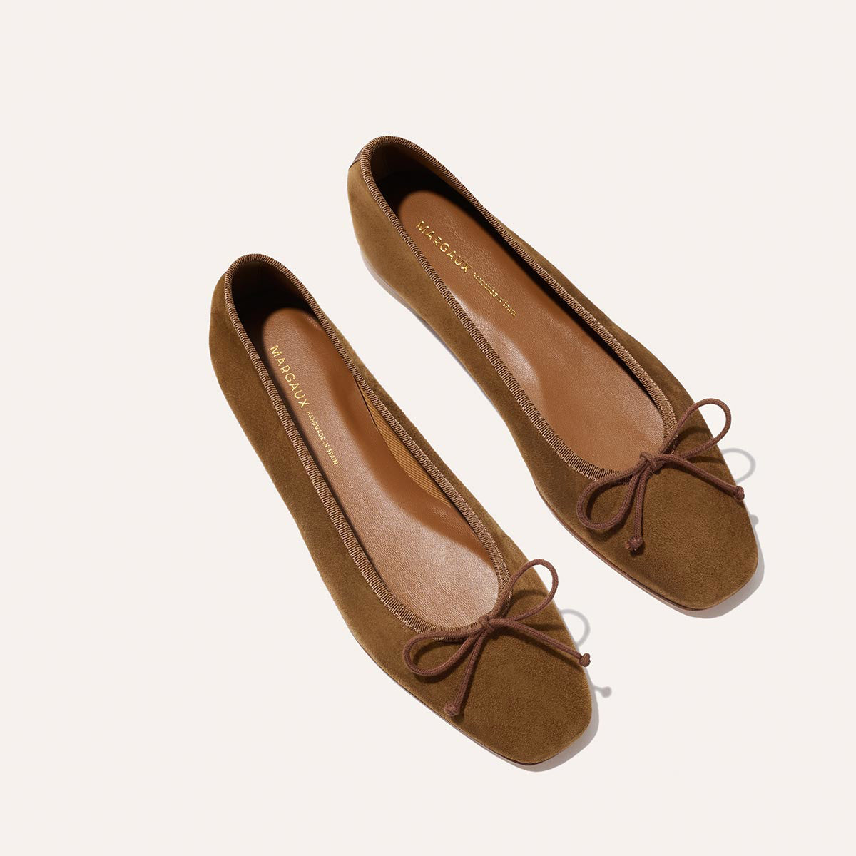 The Fonteyn - Cedar Suede by Margaux: brown suede ballet flats with square toes, handcrafted details, brown bow laces, and tan insoles, displayed on a light background.