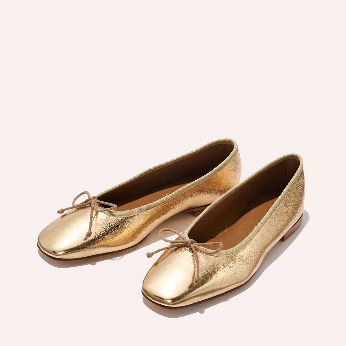 The Fonteyn - Gold Crinkle Nappa by Margaux: shiny gold ballet flats with a front bow, displayed on a plain light background.