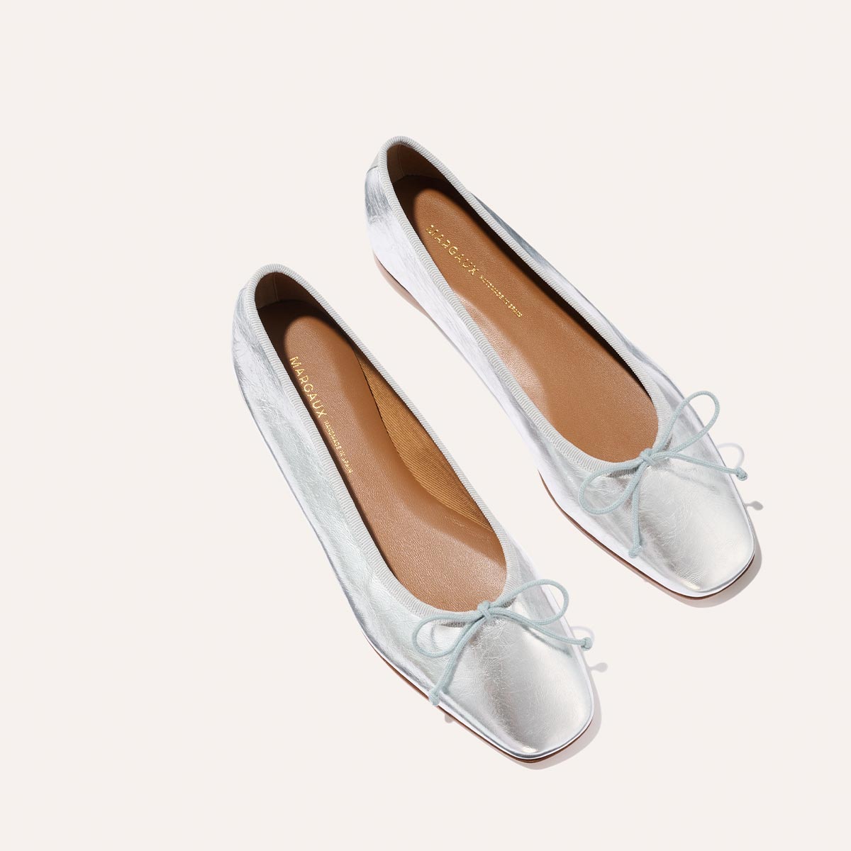 The Fonteyn - Silver Crinkle Nappa by Margaux: elegant silver ballet flats with square toes and delicate front bows, showcased against a simple light background.
