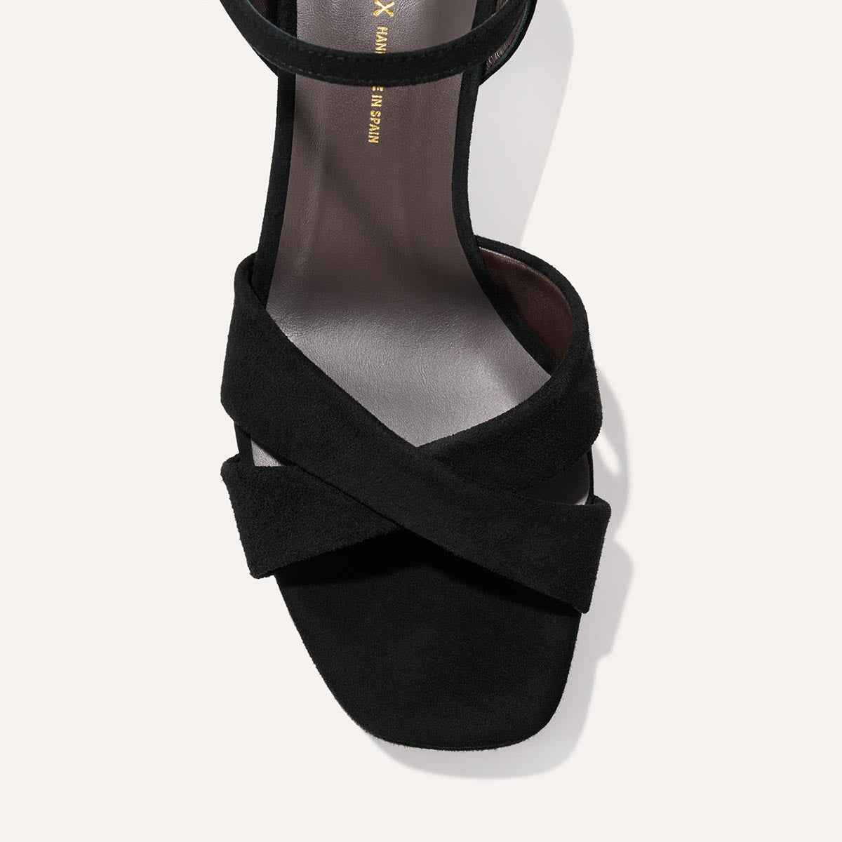 The Paloma Platform by Margaux in black suede features two wide crisscross straps over the toe, an ankle strap, and a padded platform for all-night comfort, shown close-up against a light background.