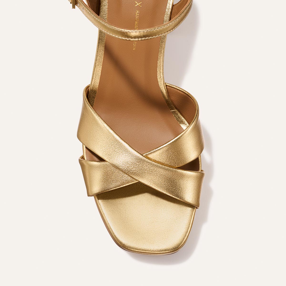 A close-up top view of Margaux’s The Paloma Platform in Gold Nappa: a strappy heeled sandal with crisscross straps, square toe, and padded platform for all-night comfort on a neutral background.