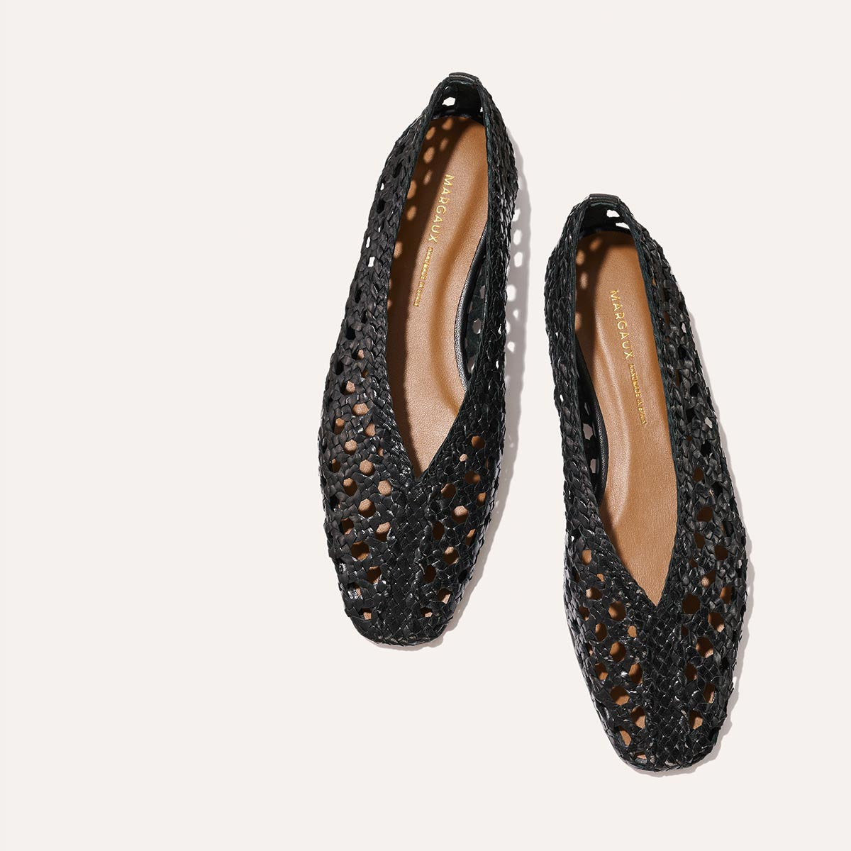 The Woven Paz - Black Leather by Margaux: a pair of handwoven black leather flats with pointed toes and open cut-out designs, displayed on a light background.