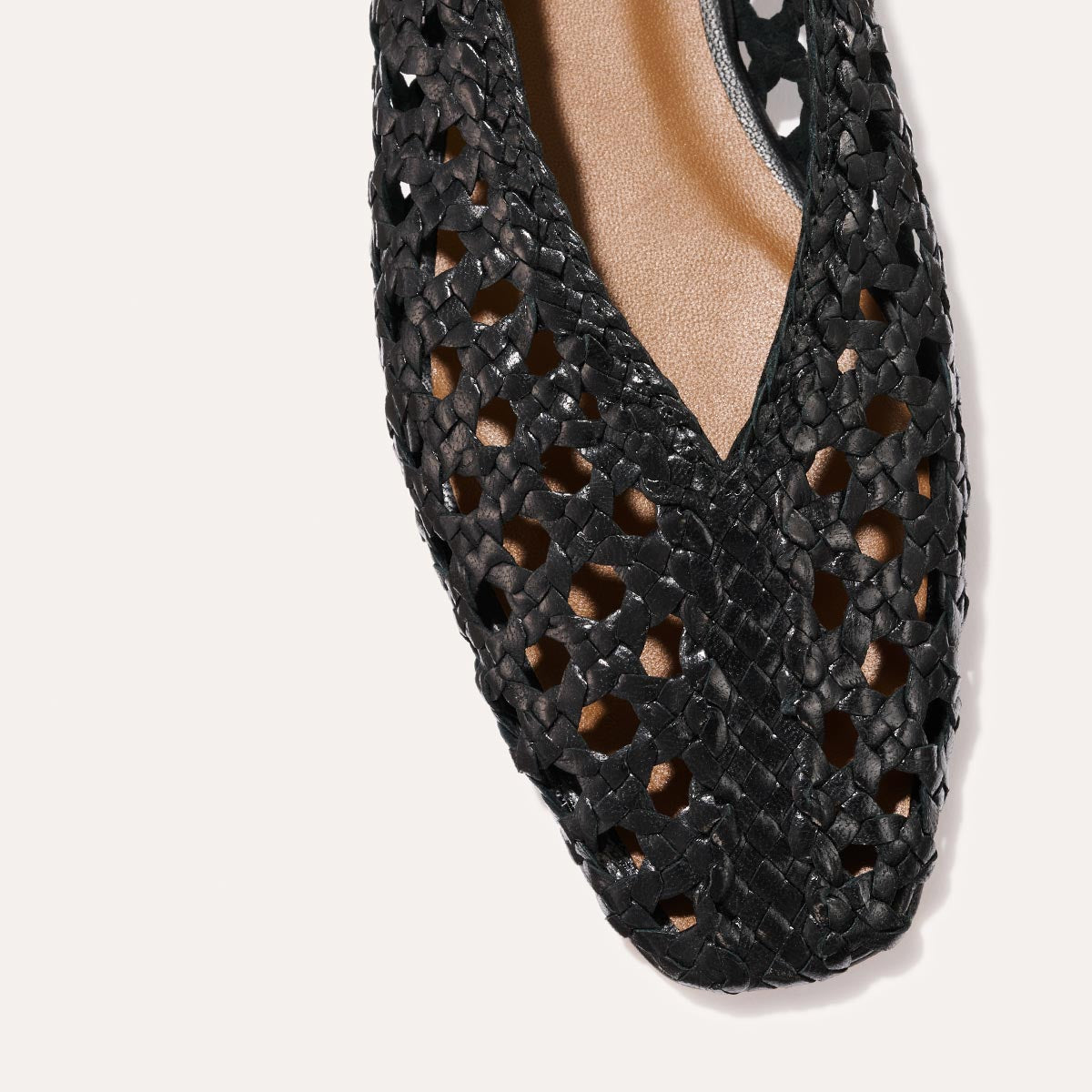 Close-up of The Woven Paz - Black Leather by Margaux, showing its pointed V-shaped opening, cutout handwoven-style upper, and a glimpse of the tan inner lining.