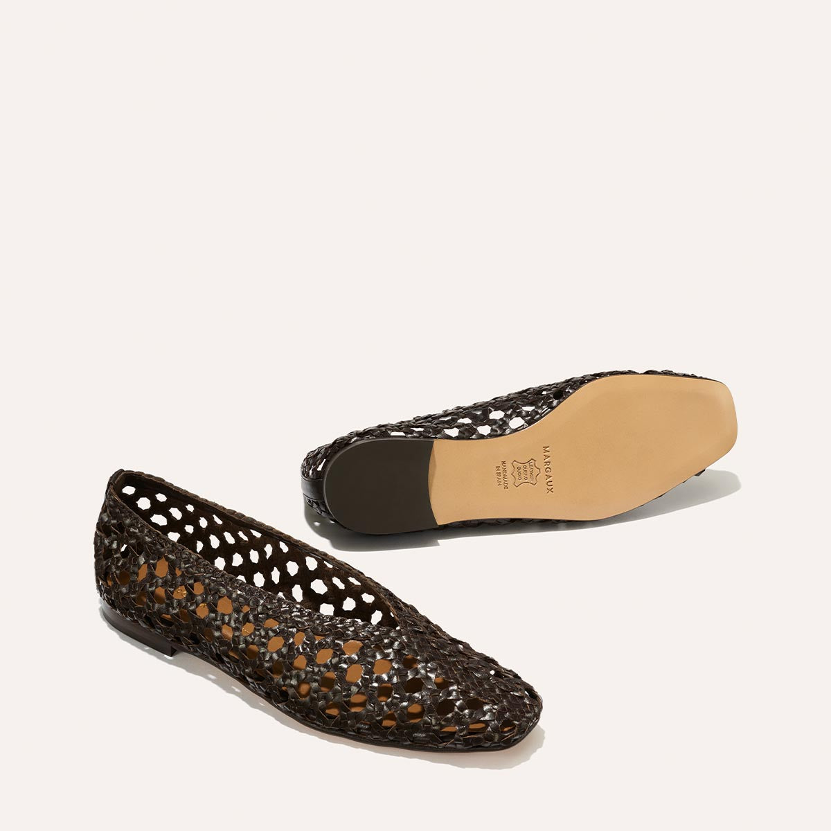 The Woven Paz flats by Margaux in espresso leather feature a luxuriously soft, handwoven openwork design and beige sole—one shown upright, the other on its side.