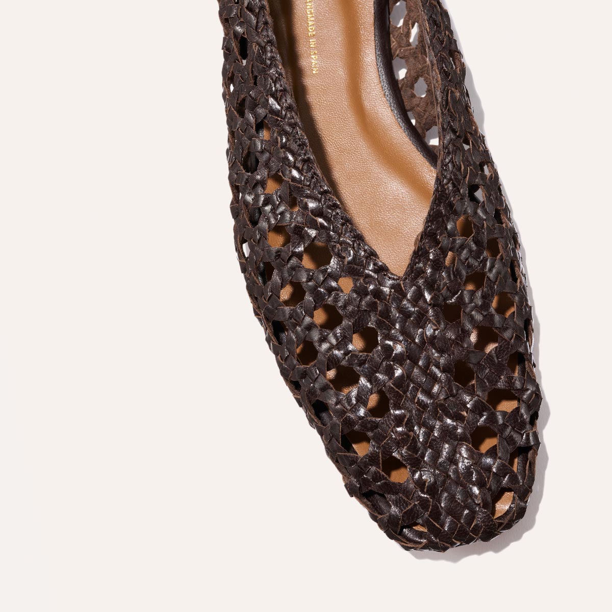 A close-up of Margaux’s The Woven Paz in Espresso Leather highlights the luxuriously soft, handwoven flat shoe with an intricate cutout pattern, showcasing expert craftsmanship against a light background.