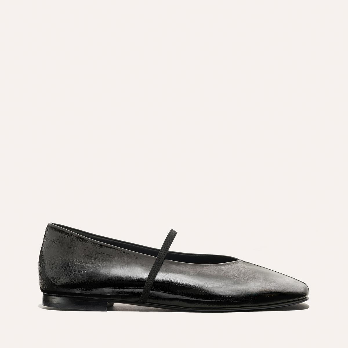 The Phoebe by margaux-development is a black crinkle-gloss nappa ballet flat featuring a thin black instep strap and sacchetto construction for extra softness, showcased on a plain light background.