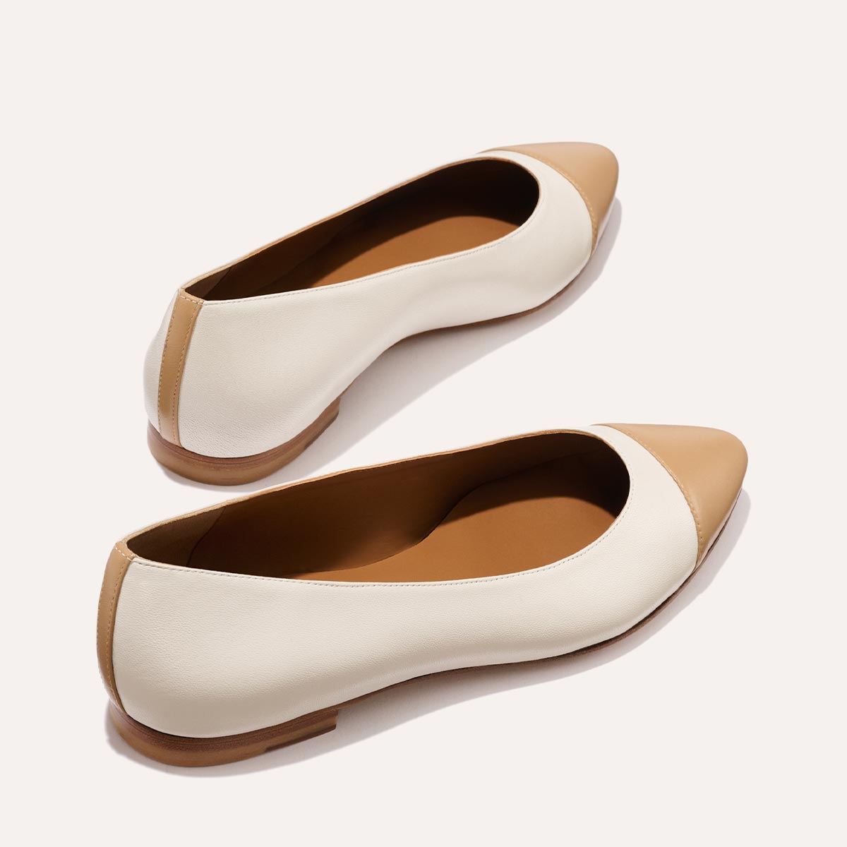 Margauxs The Pointe - Ivory and Toffee Nappa features cream bodies with tan pointed toe caps and heels in a sleek ballet flat silhouette, perfect for elevating any look, shown on a light background.