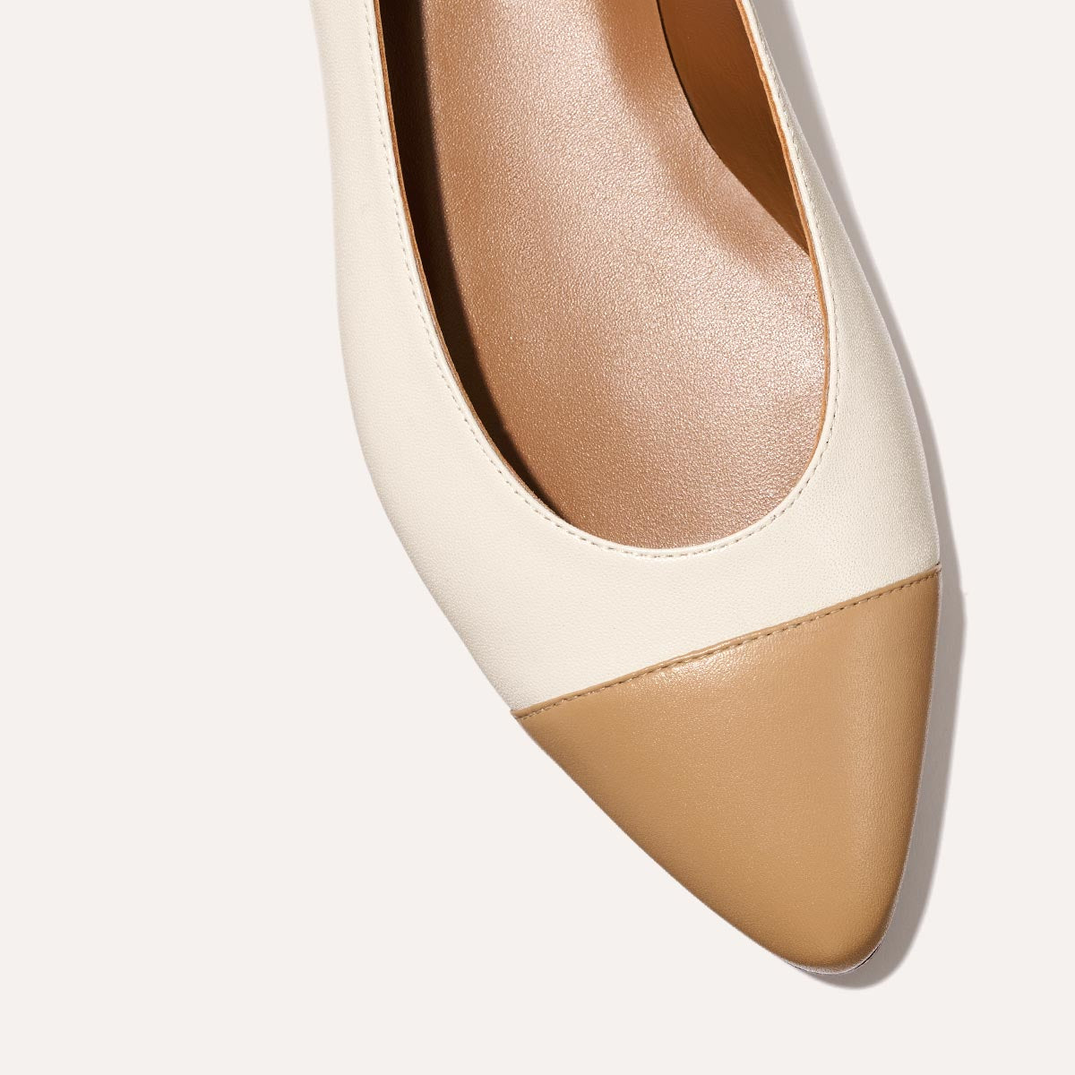 A close-up of Margaux’s The Pointe in Ivory and Toffee Nappa—a beige flat with a tan pointed toe—shown from above on a light background. This sleek silhouette elevates any look.