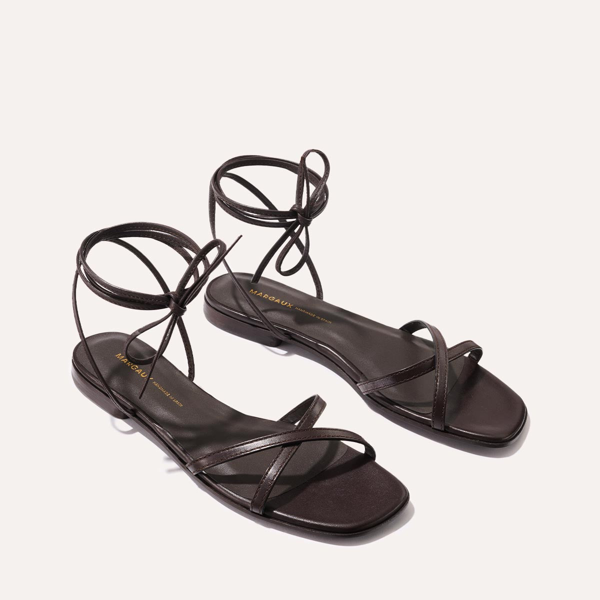 The Wrap Sandal - Espresso Nappa by Margaux features dark brown strappy styling with thin ankle ties, showcased on a neutral background—ideal for versatile summer looks.