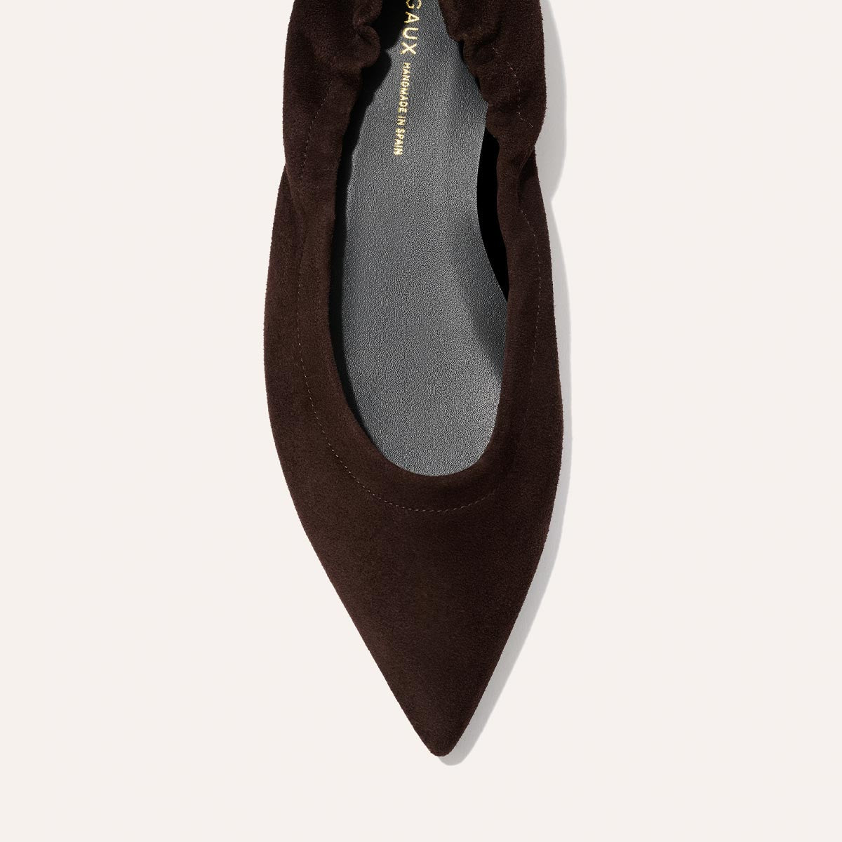 A close-up top view of Margaux’s The Roma - Espresso Suede flat, featuring a dark brown, pointed toe, ruched elastic back, and soft matte finish.