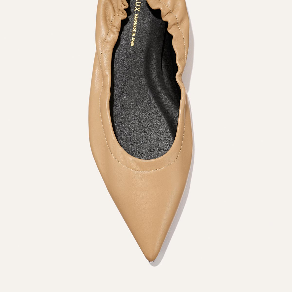 Close-up top view of The Roma - Praline Nappa flat by Margaux, featuring a beige pointed toe, ruched edge, and black insole against a plain light background.