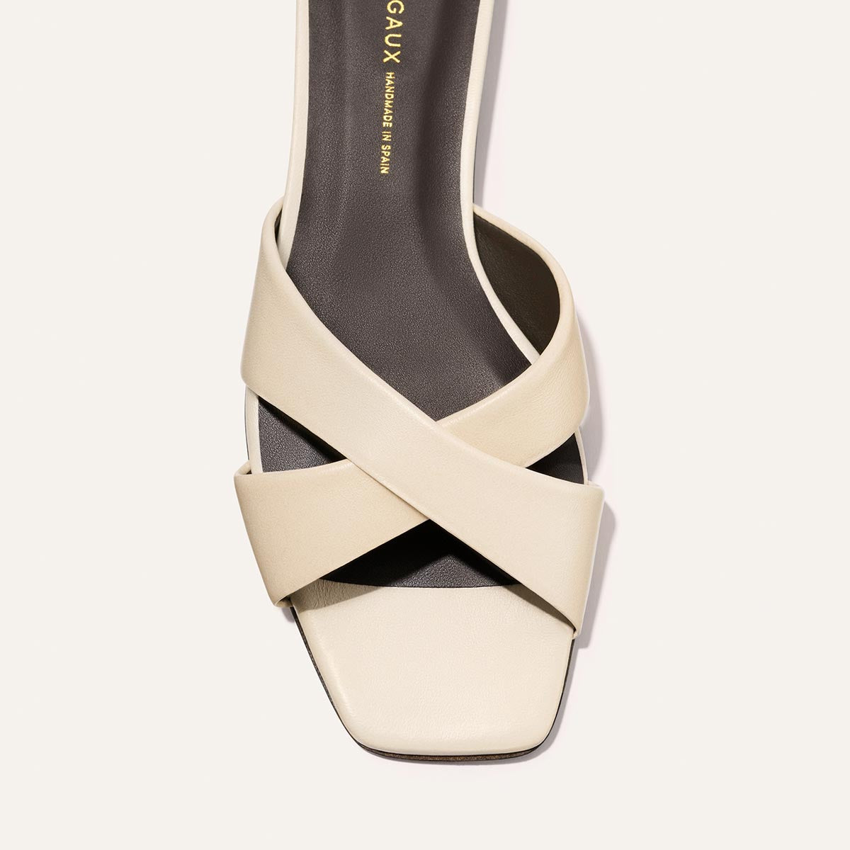 Top view of The Selene Flat Sandal - Ivoire Nappa by Margaux, featuring wide beige crisscross straps and a square toe. A dark insole with gold Margaux branding sits against a light neutral background.