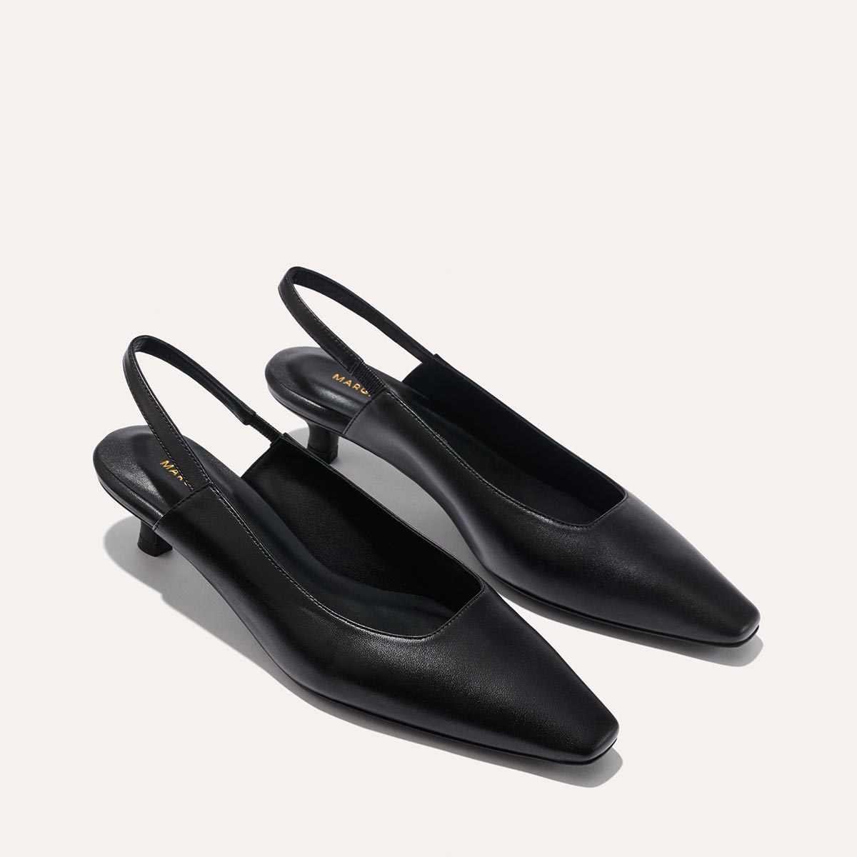 The Sofia Sling - Black Nappa by margaux-development features black slingback shoes with low micro heels and square toes, shown on a plain light background.