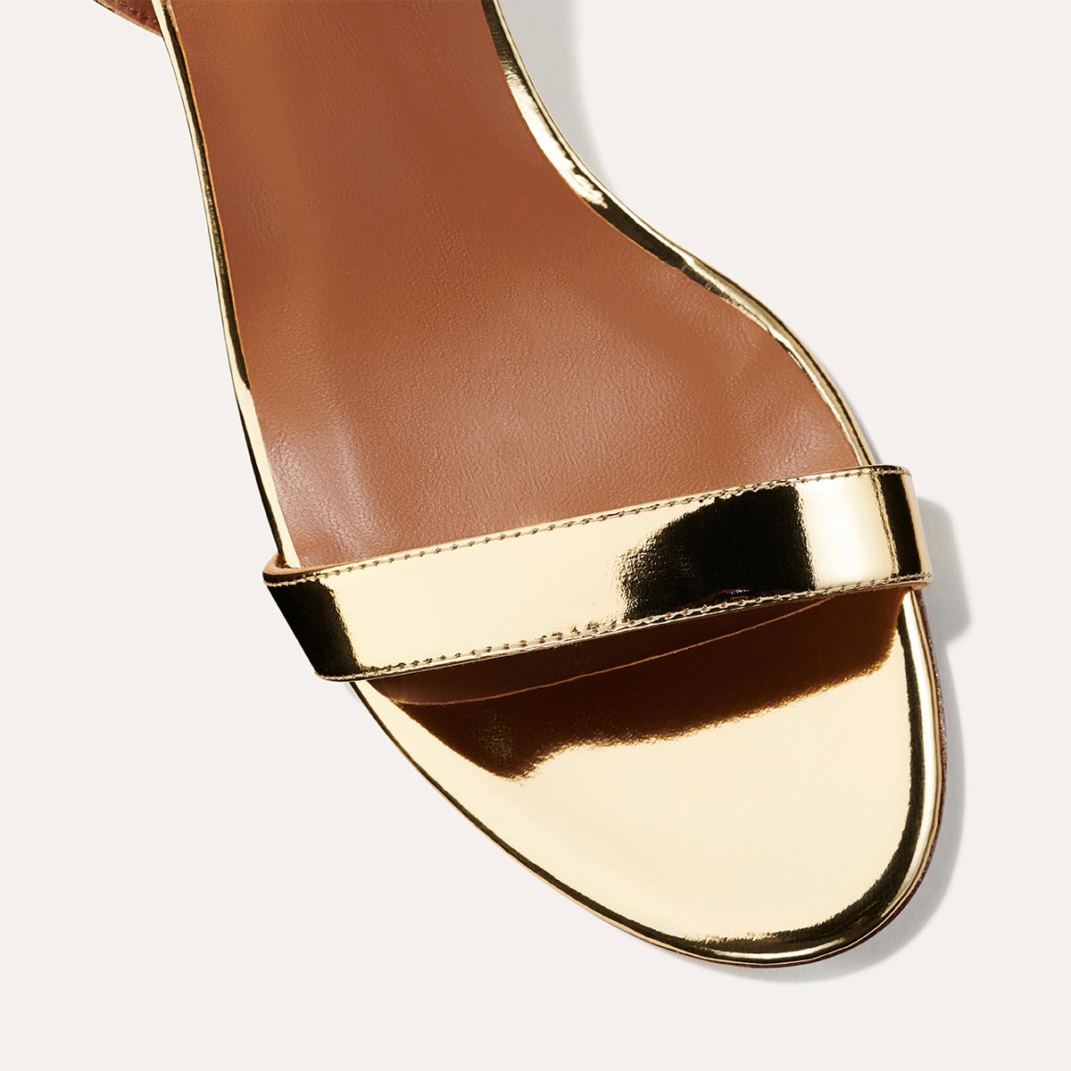 The Stella Sandal in shiny Gold Mirror, featuring a sleek strap across the toes and a comfortable 2.5-inch breasted heel.