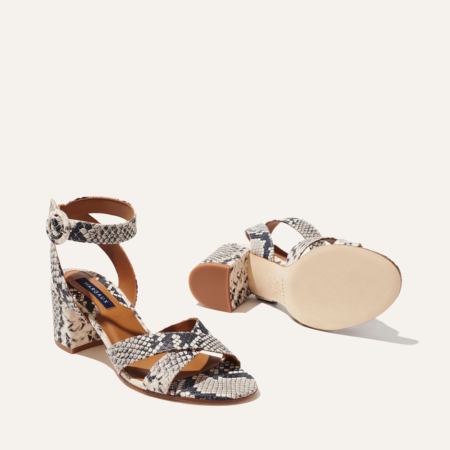 The City Sandal - Natural Python Embossed by margaux-development showcases a block heel, crisscross toe straps, ankle strap with round buckle, and cushioned insole; one sandal stands upright while the other is on its side.