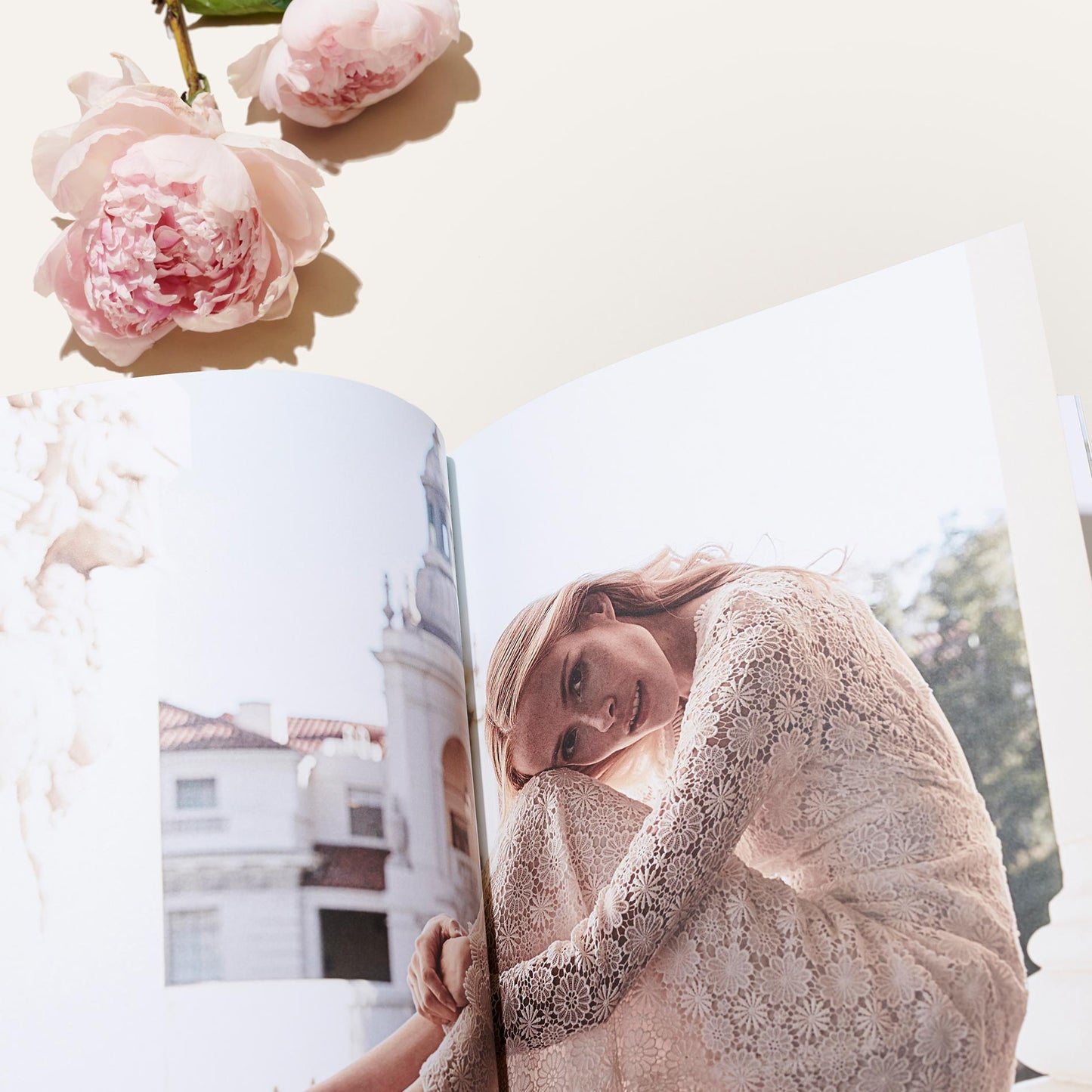 An open magazine with a photo of a woman in lace sits beside pink peonies, evoking the elegance of Margaux’s Bridal Swatch Kit on a light surface.