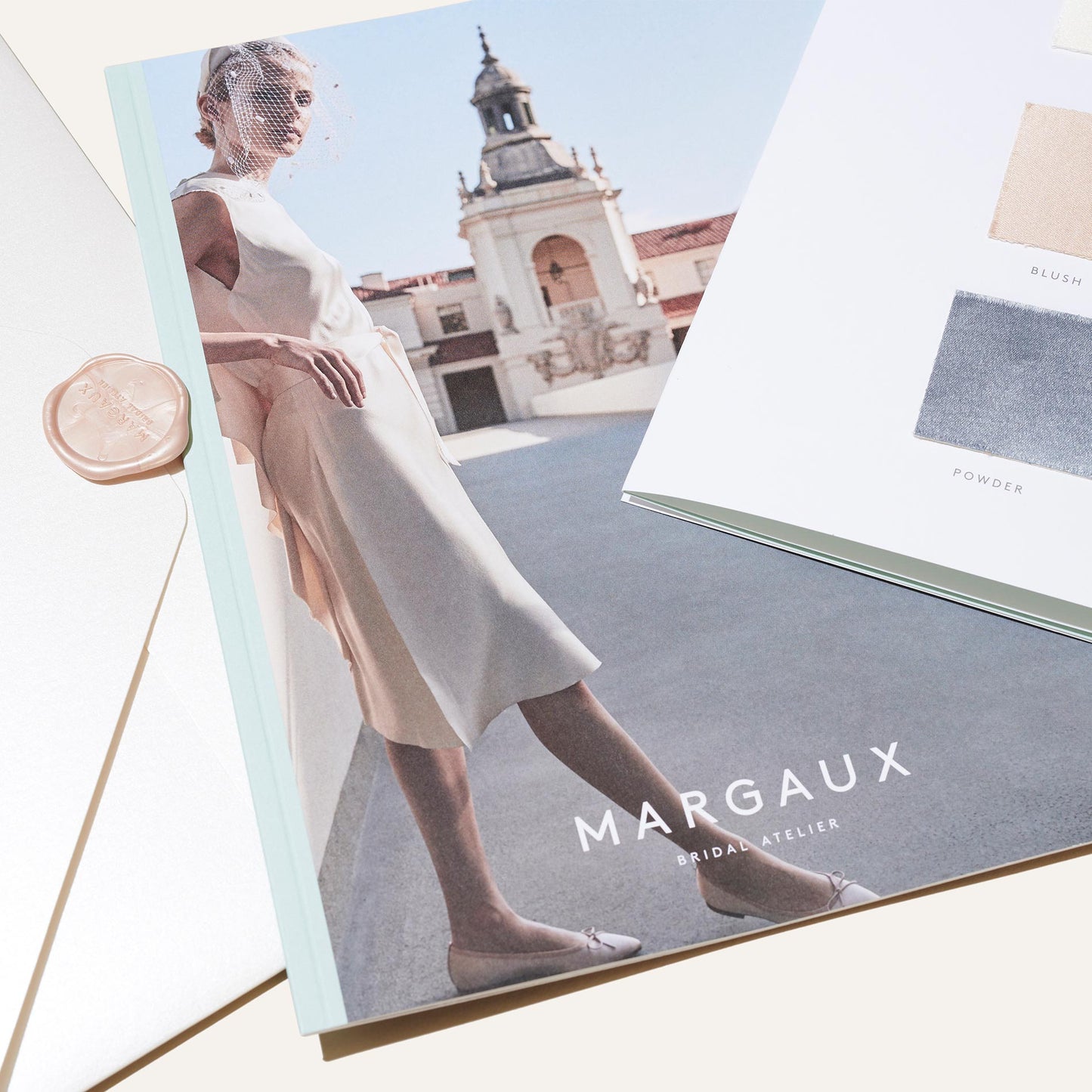 A bridal fashion magazine titled Margaux features a model in a white dress on the cover, alongside an envelope and a color sample card from the Bridal Swatch Kit by Margaux’s bespoke bridal collection.