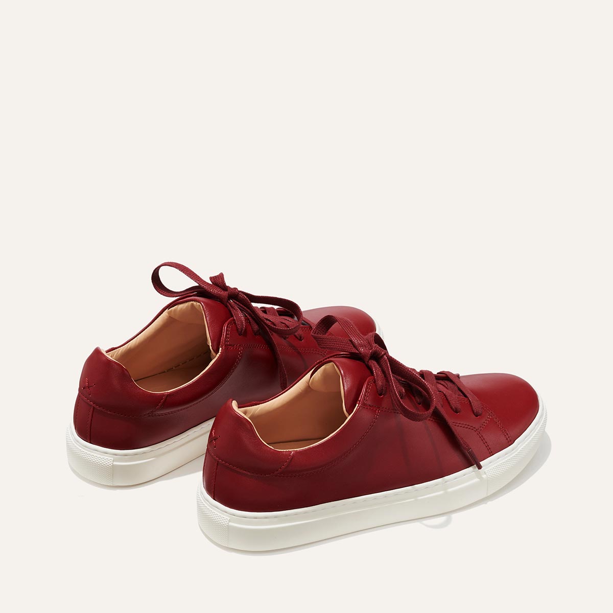 The Sneaker - Burgundy Calf by margaux-development: a pair of red leather sneakers with white rubber soles and red laces, set side by side on a simple light background.
