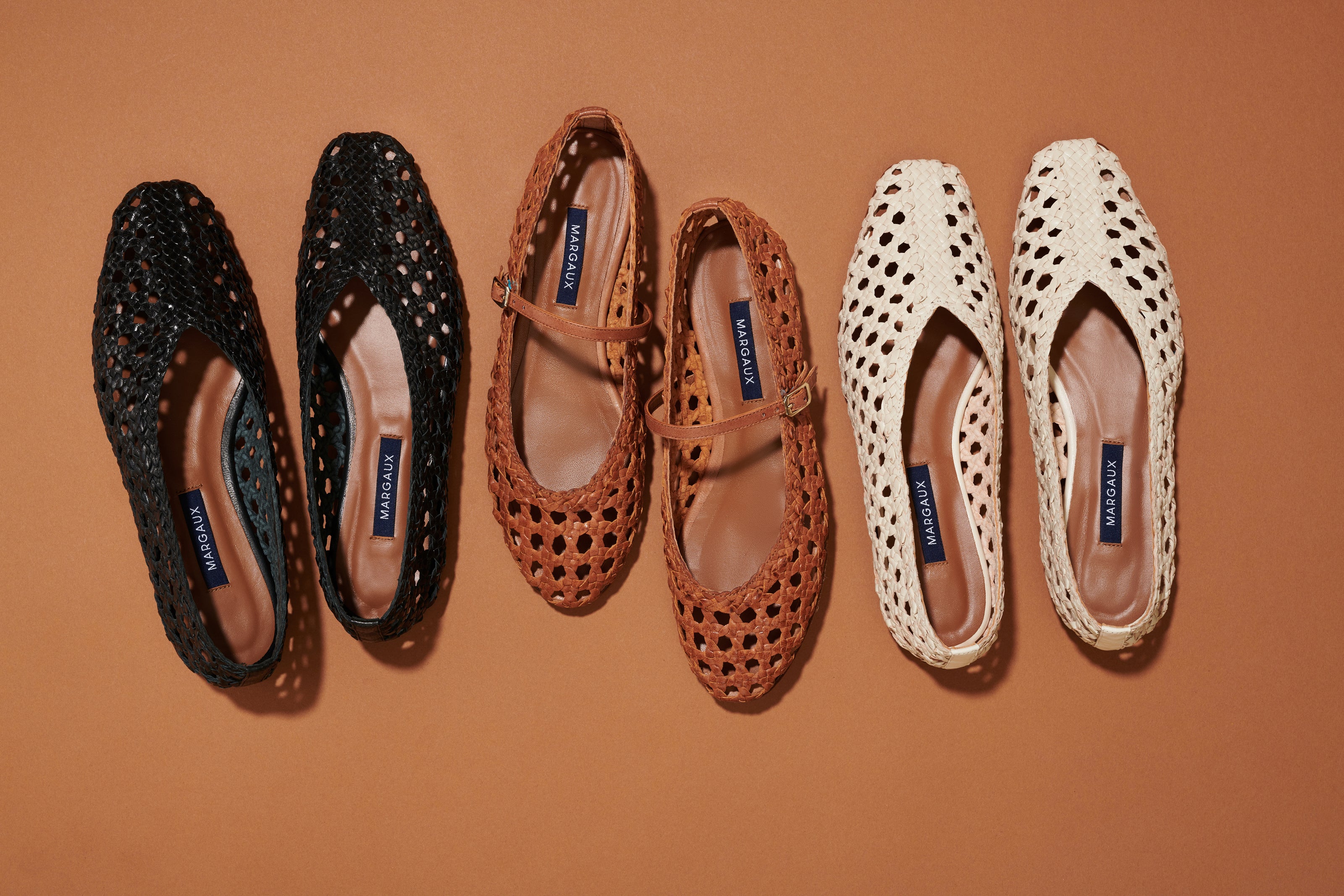 Three pairs of woven flats—black, brown with a strap, and beige—are arranged side by side on a brown background. All shoes have a MANOLO BLAHNIK label inside.