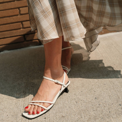 White sandals worn with plaid pants on a concrete surface.