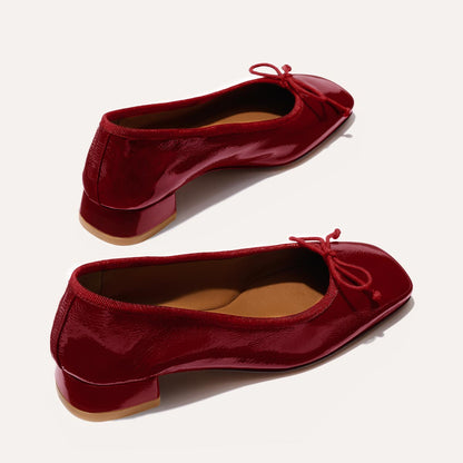The Ada in Berry Crinkle Patent, a comfortable ballet flat with a square toe, adjustable cord bow detail, and comfortable 1-inch block heel.