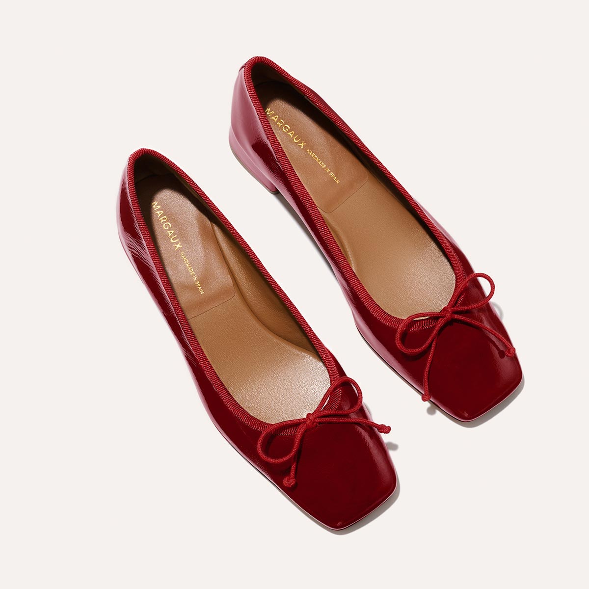 The Ada in Berry Crinkle Patent, a comfortable ballet flat with a square toe, adjustable cord bow detail, and comfortable 1-inch block heel.