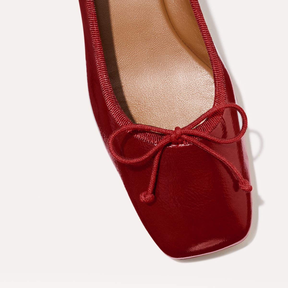 The Ada in Berry Crinkle Patent, a comfortable ballet flat with a square toe, adjustable cord bow detail, and comfortable 1-inch block heel.