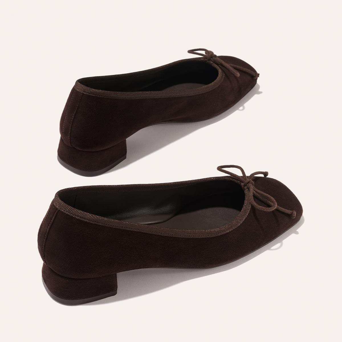 The Ada - Espresso Suede by margaux-development: dark brown suede low-heeled ballet pumps with small bows on rounded toes and a glove-like fit from sacchetto construction, displayed on a light background.
