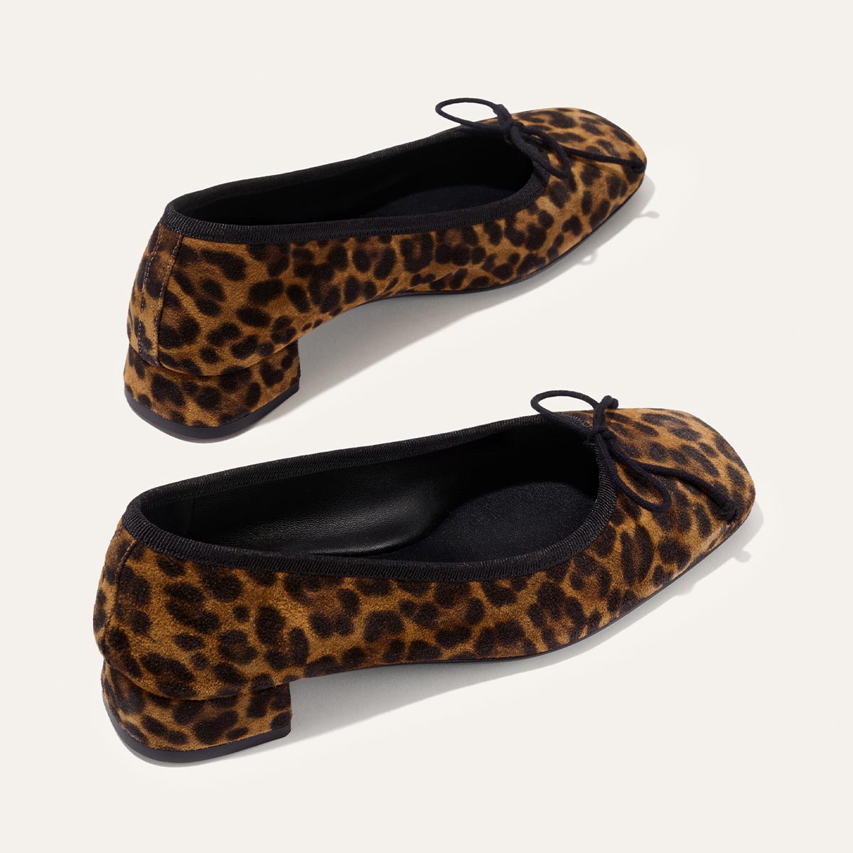 The Ada - Leopard Suede by margaux-development: leopard-print ballet pumps with low, chunky heels and small front bows, designed for a glove-like fit. Shown on a plain light background.