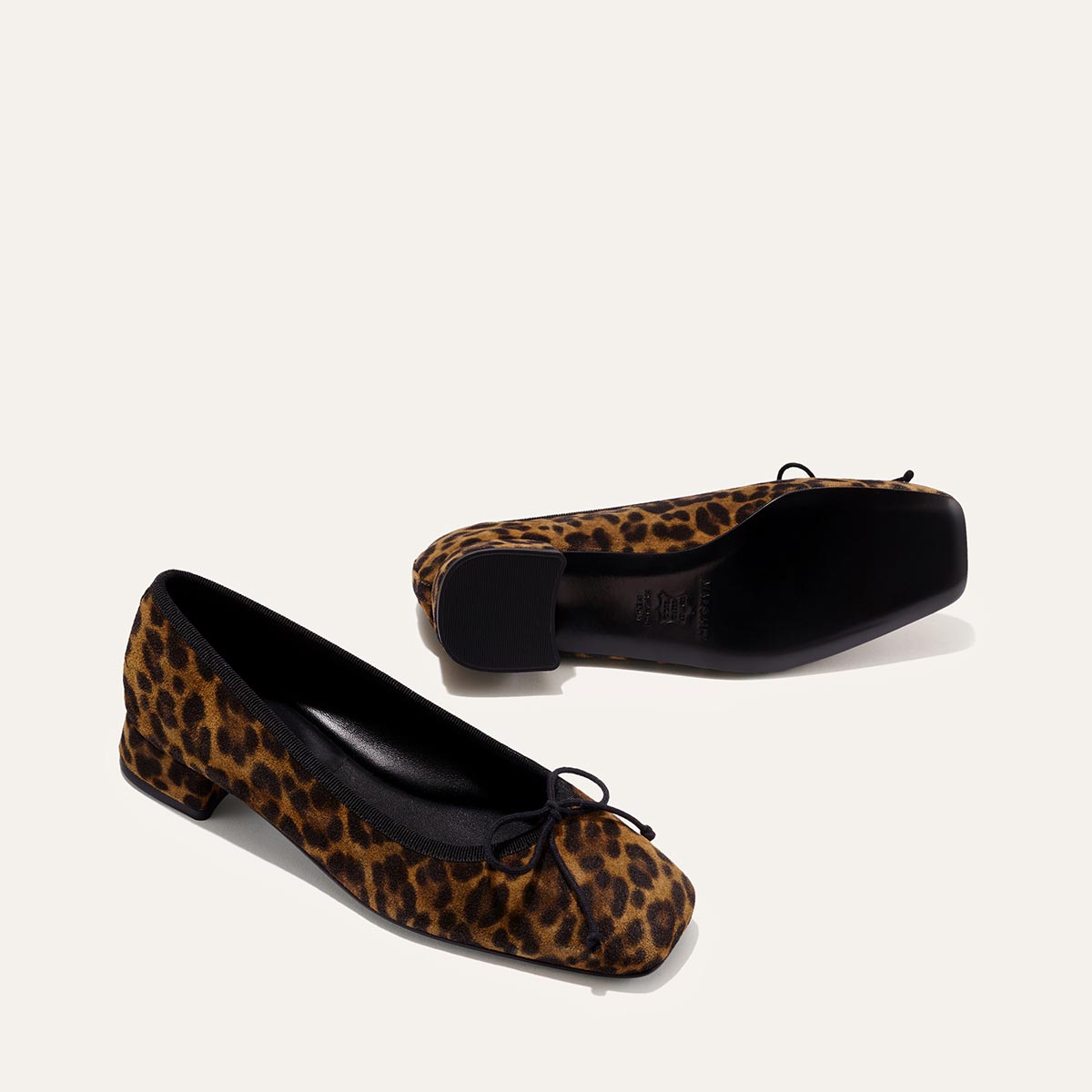 The Ada - Leopard Suede by margaux-development: leopard print, low-heeled ballet pumps with black soles, black trim, and small front bows, offering a glove-like fit with sacchetto construction, shown on a plain light background.
