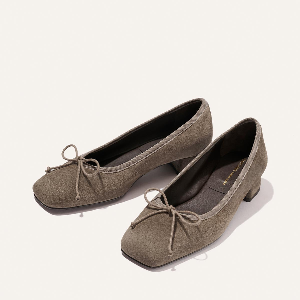 The Ada - Truffle Suede by Margaux: taupe suede ballet flats with low heels, square toes, and decorative bows, shown on a plain light background.